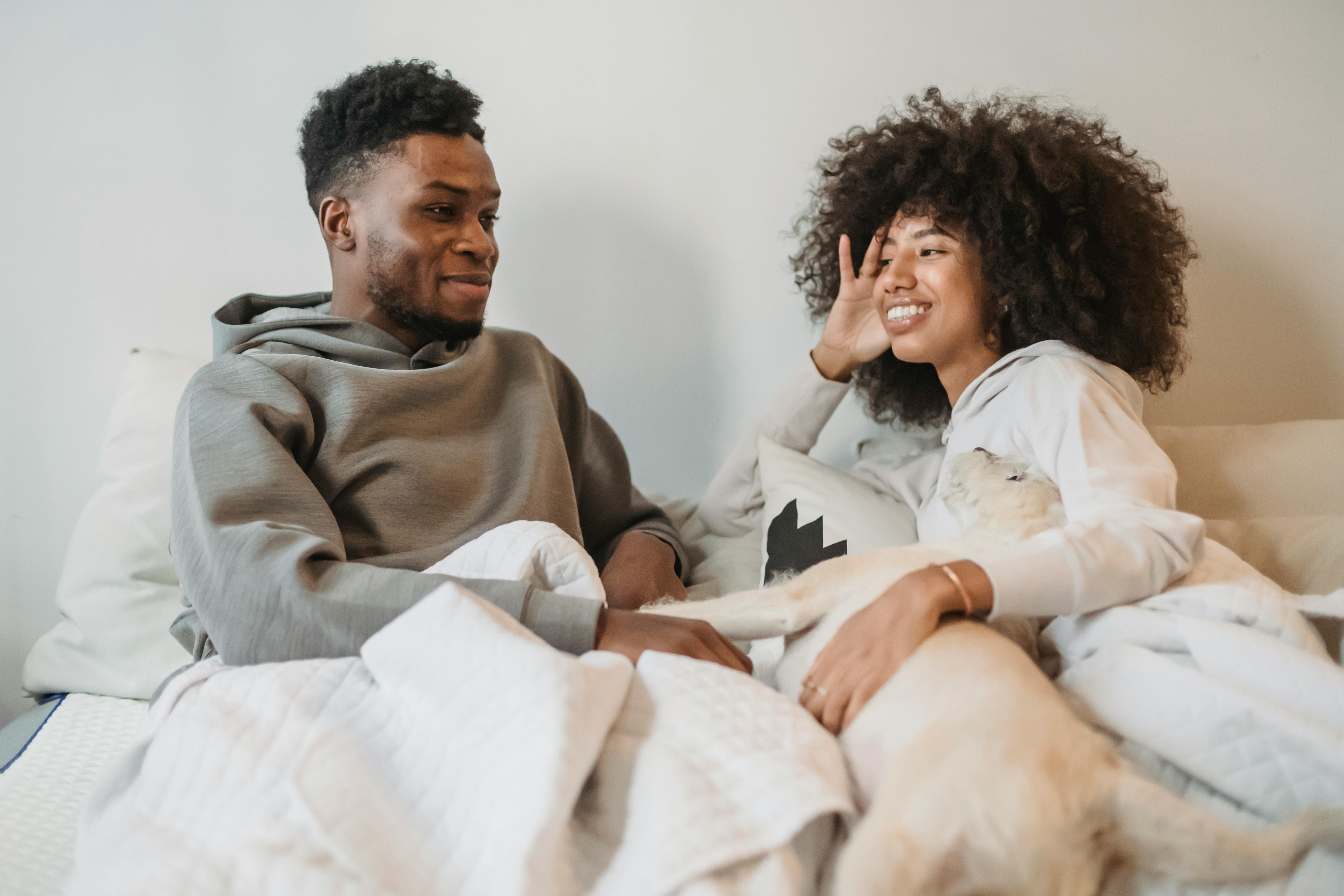 positive young black couple talking while resting on bed and caressing dog